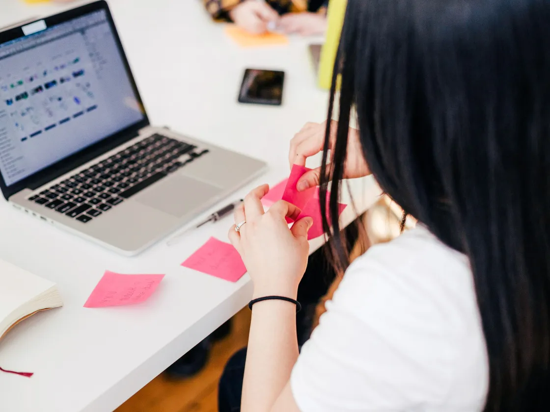 Junge Frau arbeitet mit Post-it vor dem Laptop