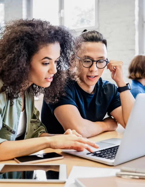 Eine junge Frau mit Locken und ein junger Mann mit Brille schauen in einen Laptop